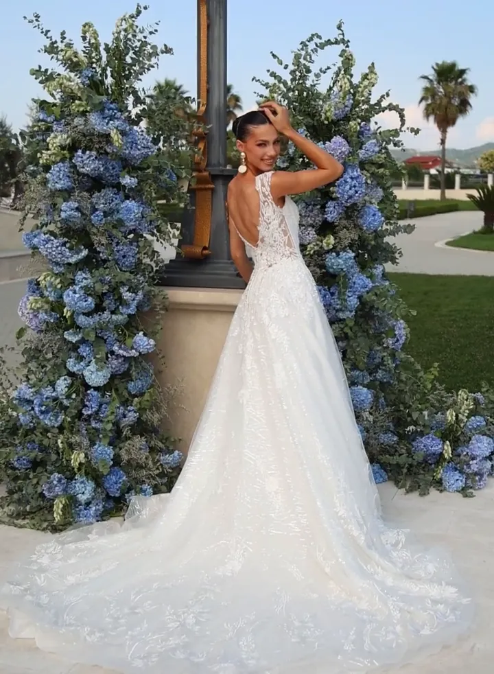Bride in a fitted ivory lace gown leaning against a stone balustrade framed by blue hydrangeas