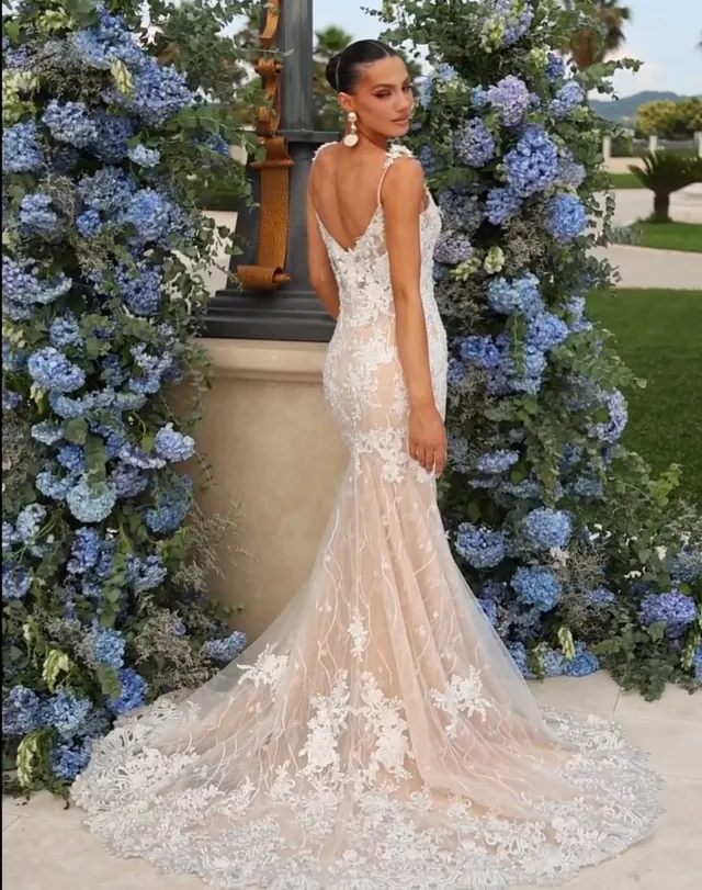 Full-length ivory lace wedding gown with a cathedral train, photographed beside blue hydrangeas