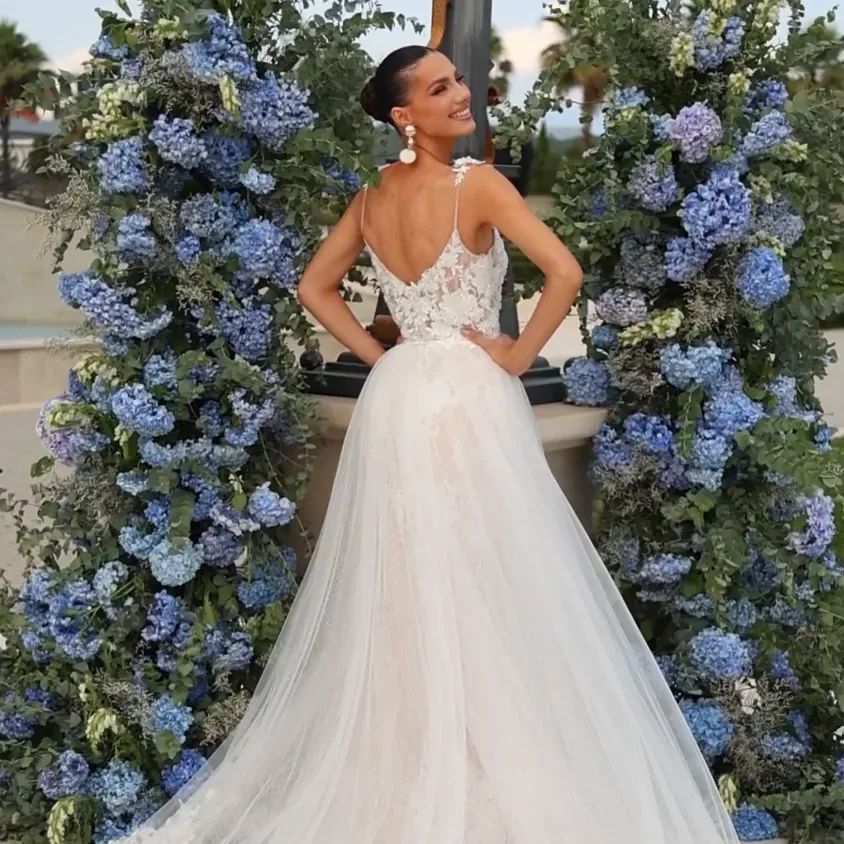 Bride in a floral lace gown with a soft tulle train, framed by blue hydrangea arrangements
